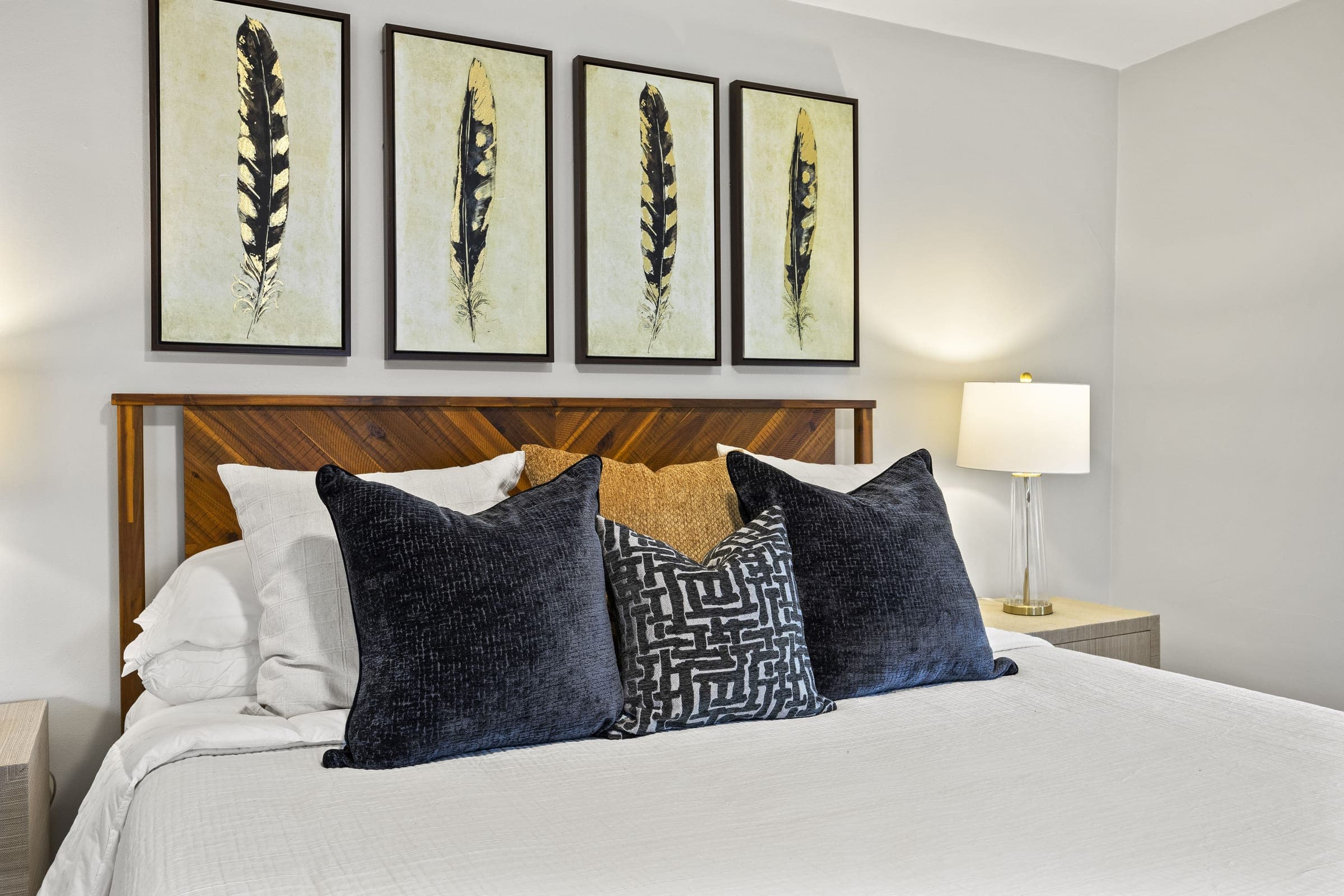 Bedroom with white bedding, navy pillows and framed feather art
